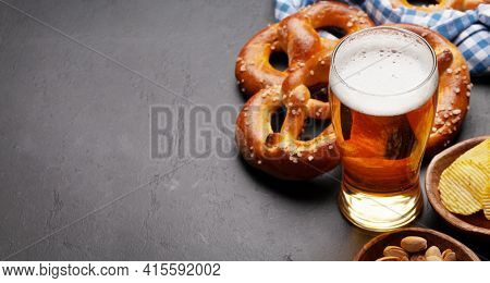 Lager beer mug, nuts, potato chips and fresh baked homemade pretzel with sea salt on stone table. Classic beer snack. With copy space