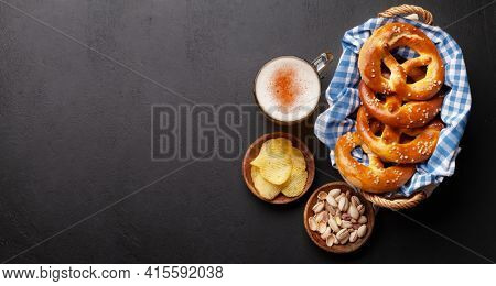 Lager beer mug, nuts, potato chips and fresh baked homemade pretzel with sea salt on stone table. Classic beer snack. Top view flat lay with copy space