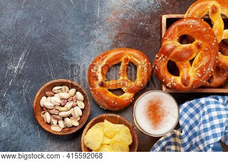 Lager beer mug, nuts, potato chips and fresh baked homemade pretzel with sea salt on stone table. Classic beer snack. Top view flat lay with copy space