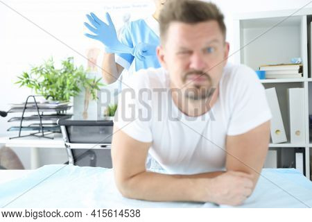Doctor Putting On Protective Glove For Rectal Examination Of Man