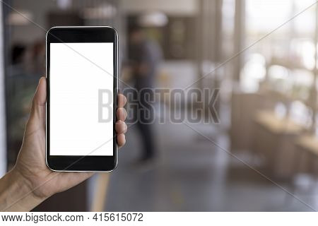 Hand Man Holding Black Mobile Phone With Blank White Screen With Blur Coffee Shop Background. Mockup