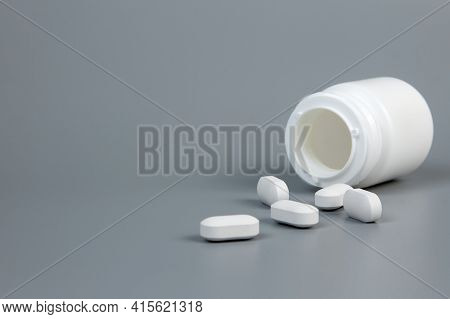 White Bottle With Scattered White Tablets On A Gray Background