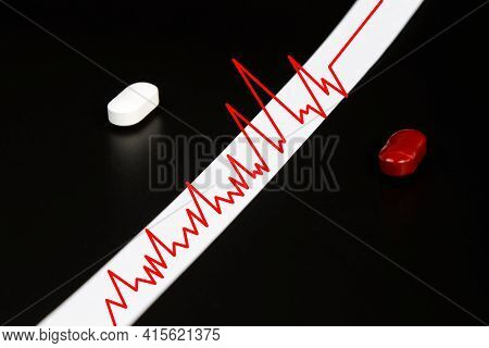 The White And Red Tablets Are Separated By A Cardiogram On A Black Background. A Concept Showing The