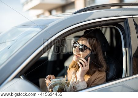 Beautiful Woman Eating Heathy Salad In The Car And Speaking On The Phone. Received A Food Order To G