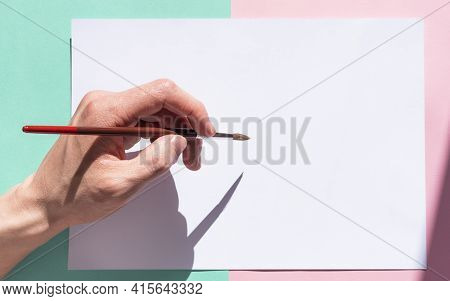 The Man Is Holding A Paint Brush With His Left Hand And Is About To Write On A Pad Of Paper. Left-ha
