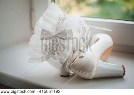 White Wedding Garter And White High Heel Shoes On The White Windowsill