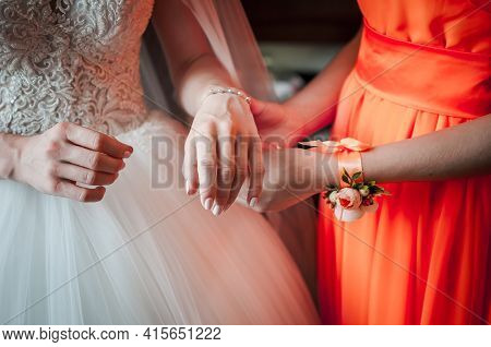 Bridesmaid In Orange Dress Helps Bride To Wear Bracelet
