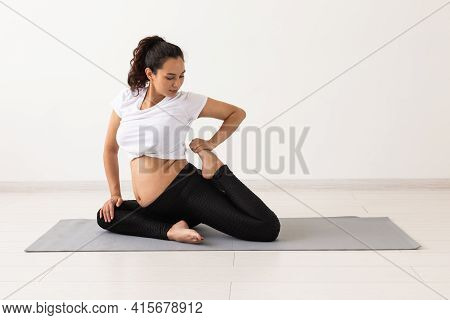 Young Flexible Pregnant Woman Doing Gymnastics On Rug On The Floor On White Background. The Concept 