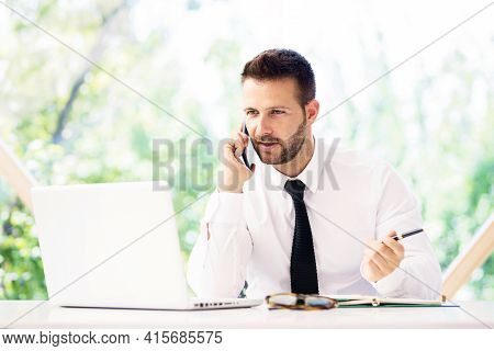 Shot Of Worried Businessman Talking With Somebody On His Mobile Phone While Sitting Behind Her Lapto