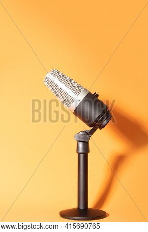 Professional Condenser Microphone With Pedestal Isolated On Orange Background Creating Shadow, Selec