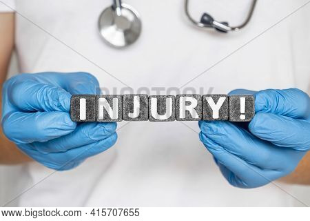 Injury - Word From Stone Blocks With Letters Holding By A Doctor's Hands In Medical Protective Glove