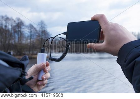 A Man Charges A Smartphone With A Power Bank. The Phone In Hand Is Being Charged With A Portable Cha