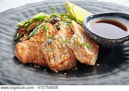 Teppanyaki Style Salmon - Grilled Salmon Fillet with Soy Sauce and Vegetables. Japanese Teppanyaki Salmon Steak garnished with lemon and green beans leaf. Black asian plate close up view
