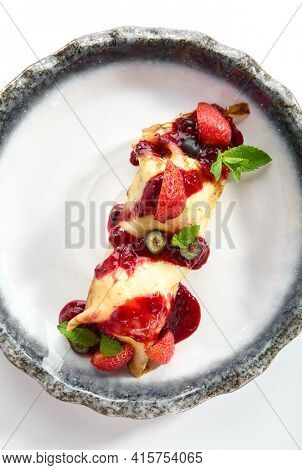 French Style Crepes - Cream Crepes with Berry and Fruit. Pancake Breakfast on white and blue plate isolated on white background. Mixed berry crepes garnished with mint and sweet sauce top view