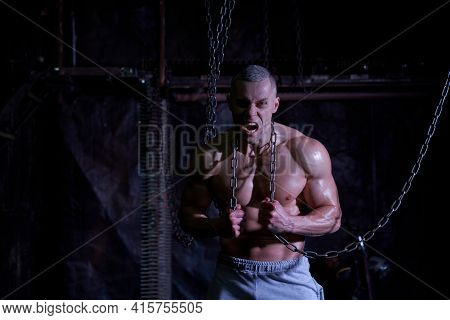 Primal Instinct. Angry Muscular Man Screaming At Camera And Breaking Chains On Chest, Dark Backgroun