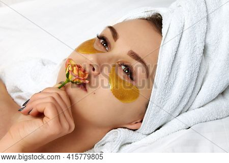 A Young Beautiful Girl With A Rose In Her Mouth With A White Towel On Her Head, Lying On A Snow-whit