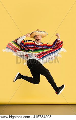 Happy Man In Sombrero And Bright Poncho Isolated Over Yellow Background
