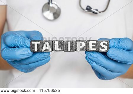 Talipes - Word From Stone Blocks With Letters Holding By A Doctor's Hands In Medical Protective Glov