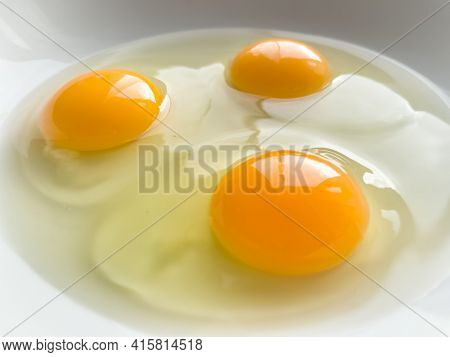 Three bright yellow raw chicken eggs in a white bowl.