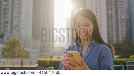 Woman use of smart phone with sun flare in city