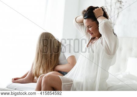 Family conflict and relations concept. Mother and daughter having quarrel and aguring at home. Sad woman and teenage girl sitting on bed. Not looking at each other.