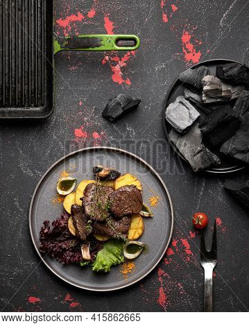 Plate Of Grilled Meat And Potatoes On Black Background Of Rustic Kitchen Table With Grill Pan And Ch