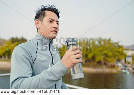 Young Sport Man Hold Water Bottle Between Jogging And Listening Music In The Park.