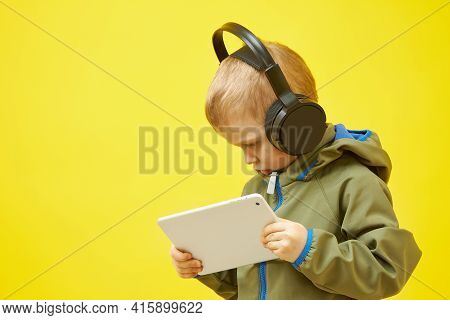 E-learning. A Small Boy With Headphones Is Studying A Tablet Computer On A Yellow Background