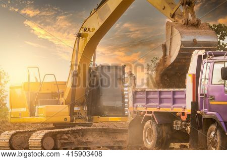 Backhoe Working By Digging Soil At Construction Site And Loading To The Truck. Bucket Of Backhoe Tra
