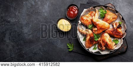 Hot barbecue chicken wings with hot sauce on plate. Top view flat lay on wide stone table. With copy space
