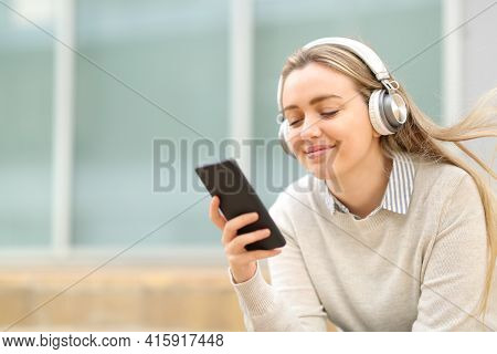 Satisfied Teen Listening To Music On Smart Phone Sitting In The Street