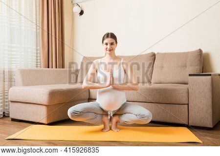 Beautiful Young Pregnant Woman Sitting On Mat In Yoga Pose At The Home. Pregnancy Yoga And Fitness C
