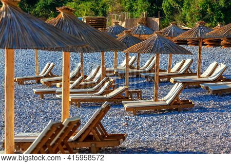 Chaise Longues With Exotic Umbrellas At The Pebble Tropical Beach