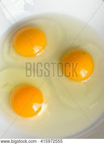 Three bright yellow raw chicken eggs in a white bowl.