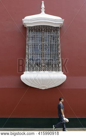 Trujillo, Peru, January 24: Unidentified Young Peruvian Man Walking In Front Of A Red Colonial Archi