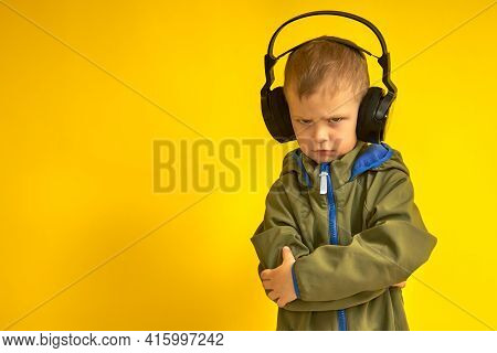 A Stern Kid In Wireless Headphones On A Yellow Background. The Child Does Not Like Music In Wireless