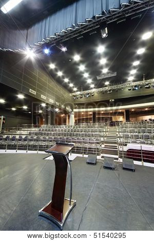 Document stand on stage and rows of seats in big black hall for business meetings. 