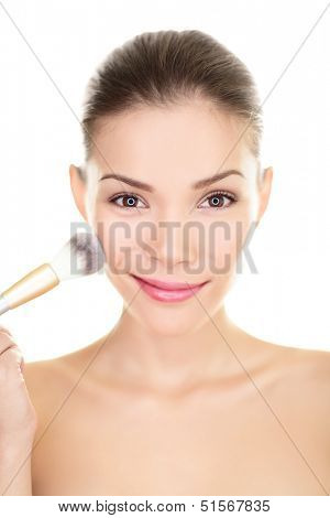 Asian beauty woman putting makeup blush on face. Chinese skincare girl applying powder with brush on cheeks, closeup smiling at camera. Mixed race Chinese Asian / Caucasian model isolated on white.