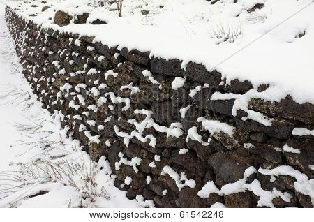 Rustic volcanic rock wall covered in snow, in Etna Park, Sicily.