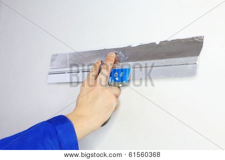 Hand of worker in blue clothes working by applicator in new apartment