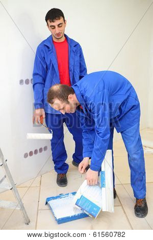Two workers in blue clothes prepare for paintind wall in new apartment