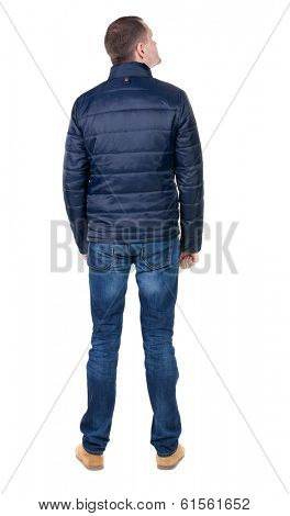Back view of handsome man in blue windcheater looking. Standing young guy in jeans. Rear view people collection.  backside view of person.  Isolated over white background.