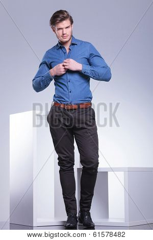 smiling casual young man buttoning his shirt, full body picture in studio