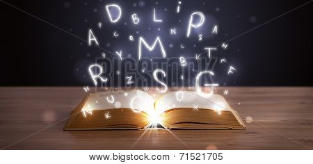 Open book with glowing letters flying out on wood deck