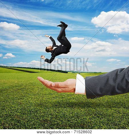 big palm catching small scared businessman over green field and blue sky