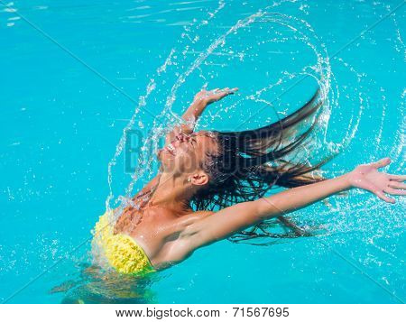 Attractive fit young tanned girl throwing wet hair back in swimming pool
