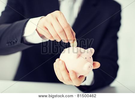 picture of man putting coin into small piggy bank