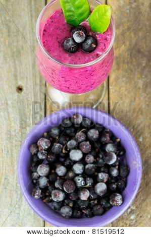 Milkshake with black currants in a glass against the background of wooden boards