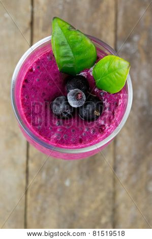Milkshake with black currants in a glass against the background of wooden boards