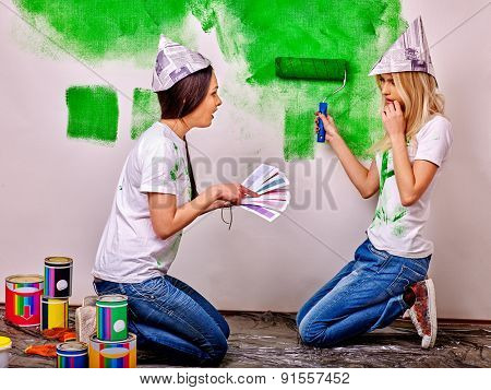 Happy woman in homamade newspaper hat paint wall at home.
